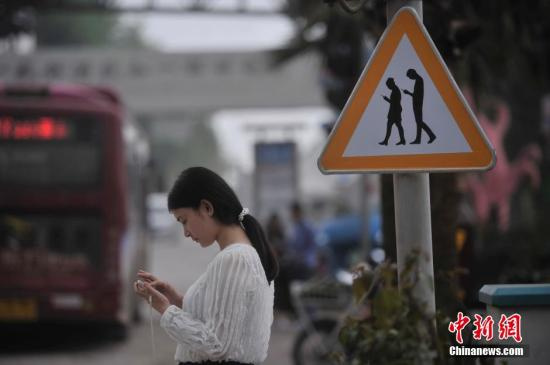 资料图：重庆涪陵红酒小镇一红绿灯处摆放了“不做低头族、关注红绿灯”警示牌，提醒市民在过斑马线的时候不能玩手机，注意交通安全。 陈超 摄
